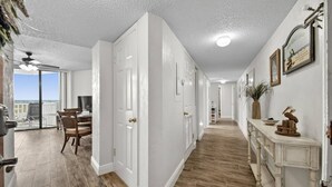 Un couloir donnant sur un balcon, un coin repas et un autre couloir avec une porte blanche et un meuble décoratif.