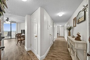 A hallway with a view to a balcony, a dining area, and a hallway with a white door and a decorative cabinet.
