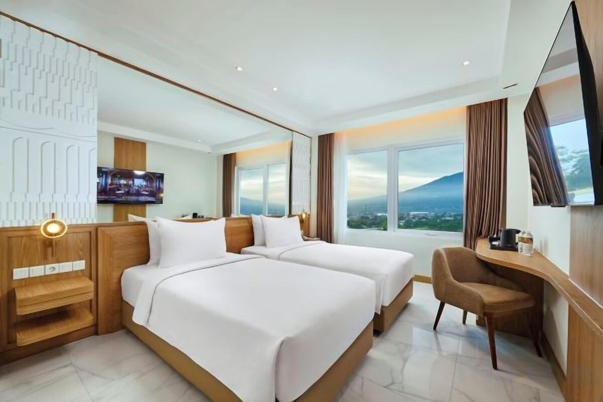 A hotel room with two beds, a desk, a TV, and a large window with a view.
