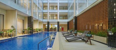 A multi-level indoor swimming pool with lounge chairs and potted plants.