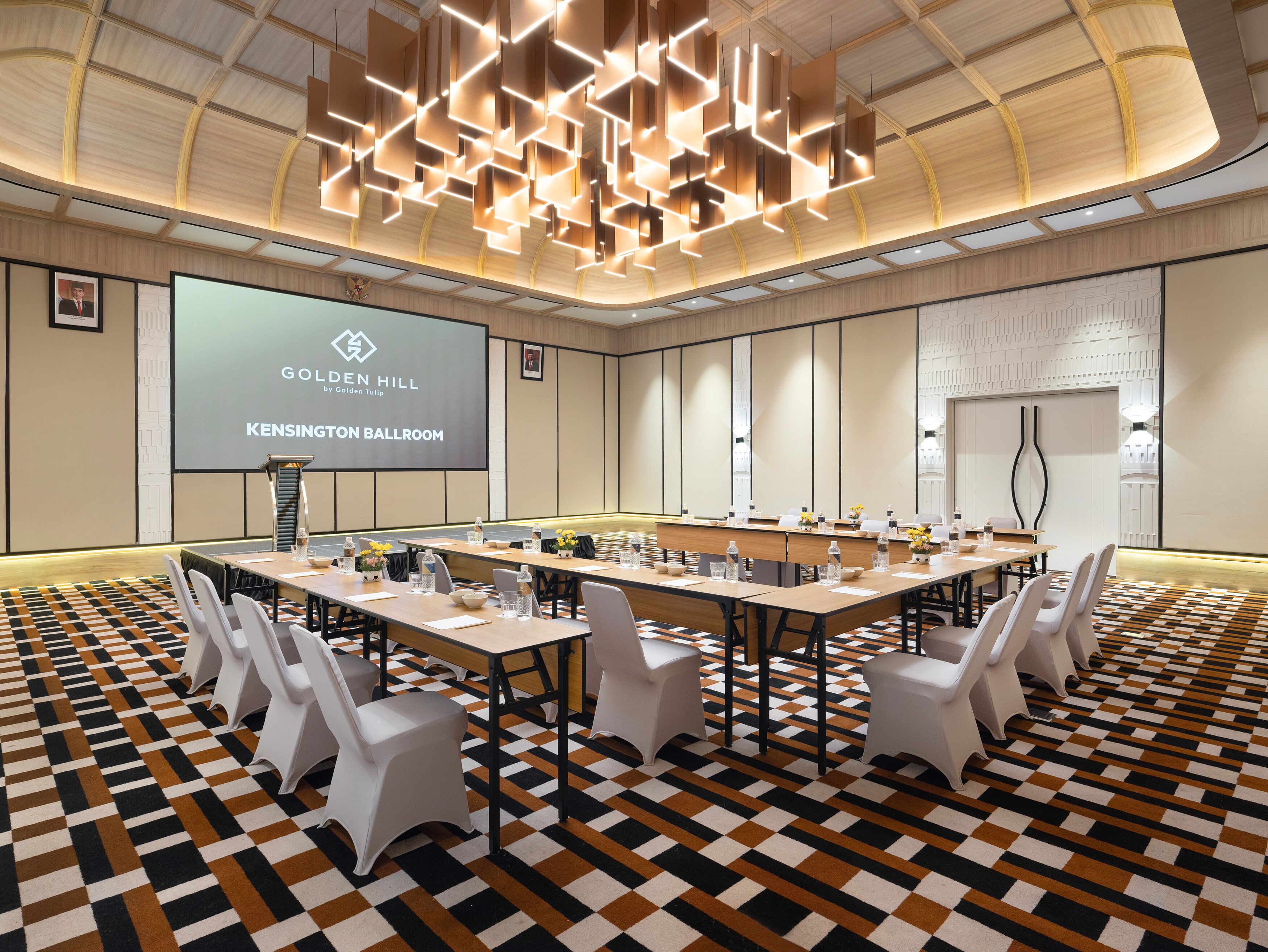 A conference room with a long table, white chairs, and a projector screen displaying "Golden Hill KENSINGTON BALLROOM".