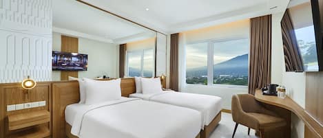 A hotel room with two beds, a desk, a chair, a TV, and a large window with a mountain view.