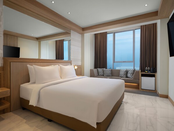 A modern hotel room with a large bed, a seating area with cushions, a flat-screen TV, and a view of the city.