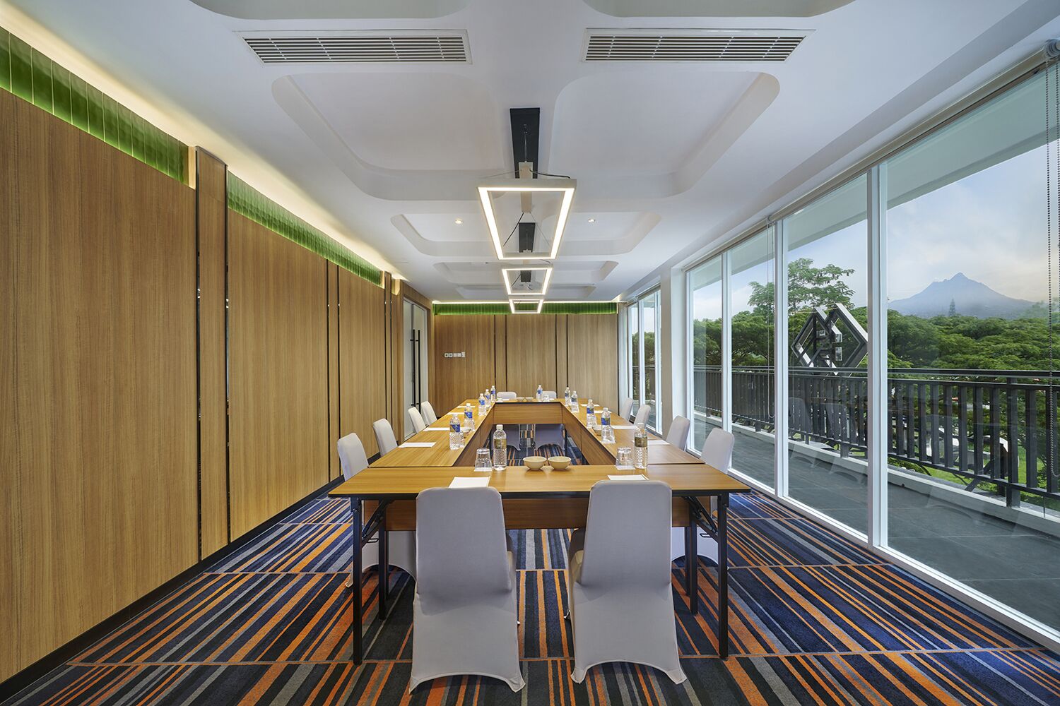Un salón de conferencias con una larga mesa, sillas y vistas a un paisaje montañoso a través de amplias ventanas.