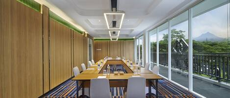 Un salón de conferencias con una larga mesa, sillas y vistas a un paisaje montañoso a través de amplias ventanas.