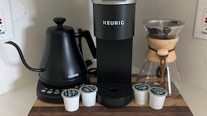 A coffee maker setup with a Keurig machine, a Cosori coffee pot, and a glass carafe with a wooden handle.