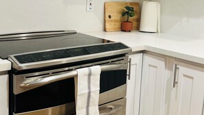 A kitchen with white cabinets, a stainless steel oven, and a wooden cutting board with a potted plant.