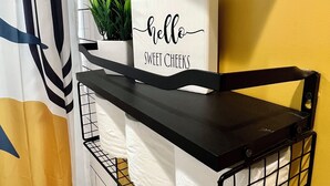 A room with a black metal shelf holding a potted plant and a sign that reads "hello sweet cheeks".