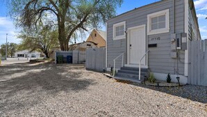 A small, single-story mobile home with a white door and windows, a gravel driveway, and a fenced yard. - Tranquil Retreat: Cozy 2Bed, 1Bath Oasis in Fallon (Fallon)