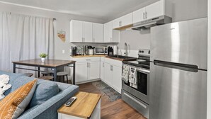 A compact kitchen with white cabinets, a stainless steel refrigerator, a microwave, and a stove. There is a wooden table with chairs and a small rug on the floor. - Tranquil Retreat: Cozy 2Bed, 1Bath Oasis in Fallon (Fallon)