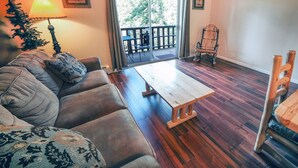 A cozy living room with a sofa, a wooden coffee table, and a rocking chair. A sliding glass door leads to an outdoor deck. - Fawn Valley Inn: 298 1 Bedroom Condo (Estes Park)