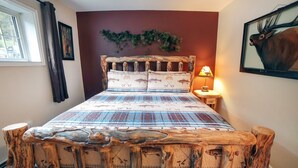 A bed with a unique wooden frame, a patterned bedspread, a wall-mounted lamp, and a framed picture on the wall. - Fawn Valley Inn: 298 1 Bedroom Condo (Estes Park)