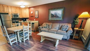 A cozy living room with a sofa and a dining table, wooden flooring, and a kitchen area with appliances. - Fawn Valley Inn: 298 1 Bedroom Condo (Estes Park)
