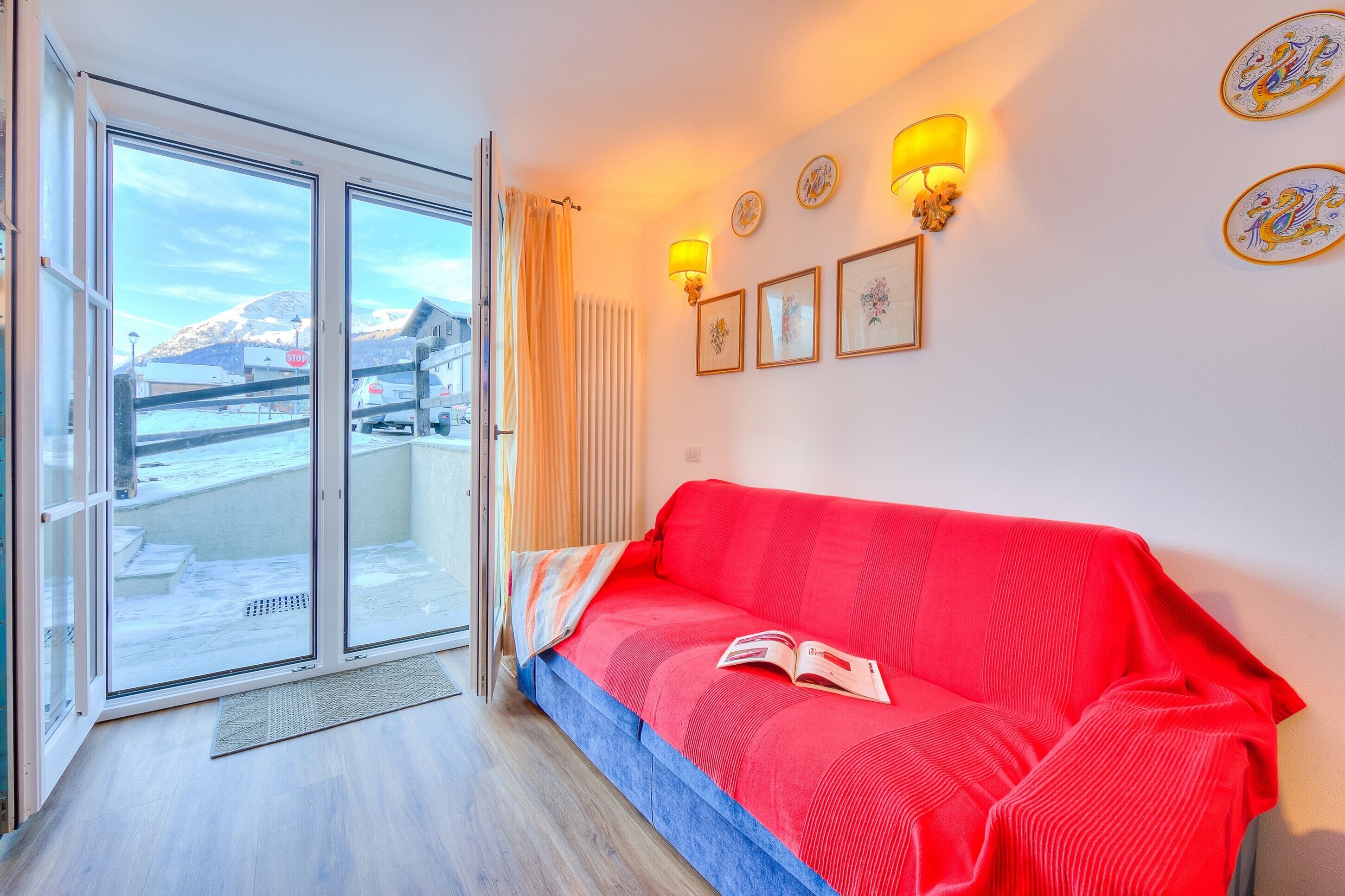 A room with a red sofa, a glass door leading outside, and wall-mounted lamps.