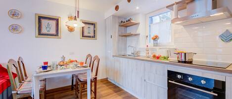 A modern kitchen with white cabinetry, a built-in oven, and a dining area with a table and chairs.