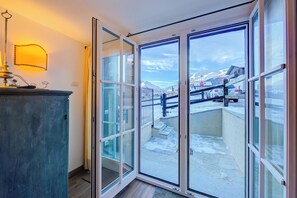 A room with a sliding glass door leading to a balcony with a view of a snowy mountain and parked cars.