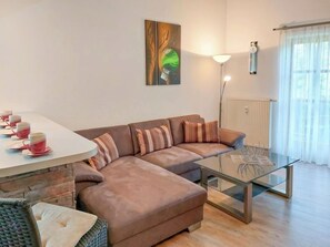A modern living room with a brown sofa, a glass coffee table, and a dining table with red cups.