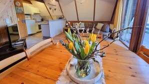 Un interior de madera acogedor con un área de comedor que incluye una mesa con un florero. Se observa una cocina al fondo.