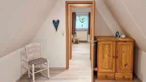 Un estrecho habitación en el ático con un armario de madera, una silla blanca y una decoración con forma de corazón en la pared.