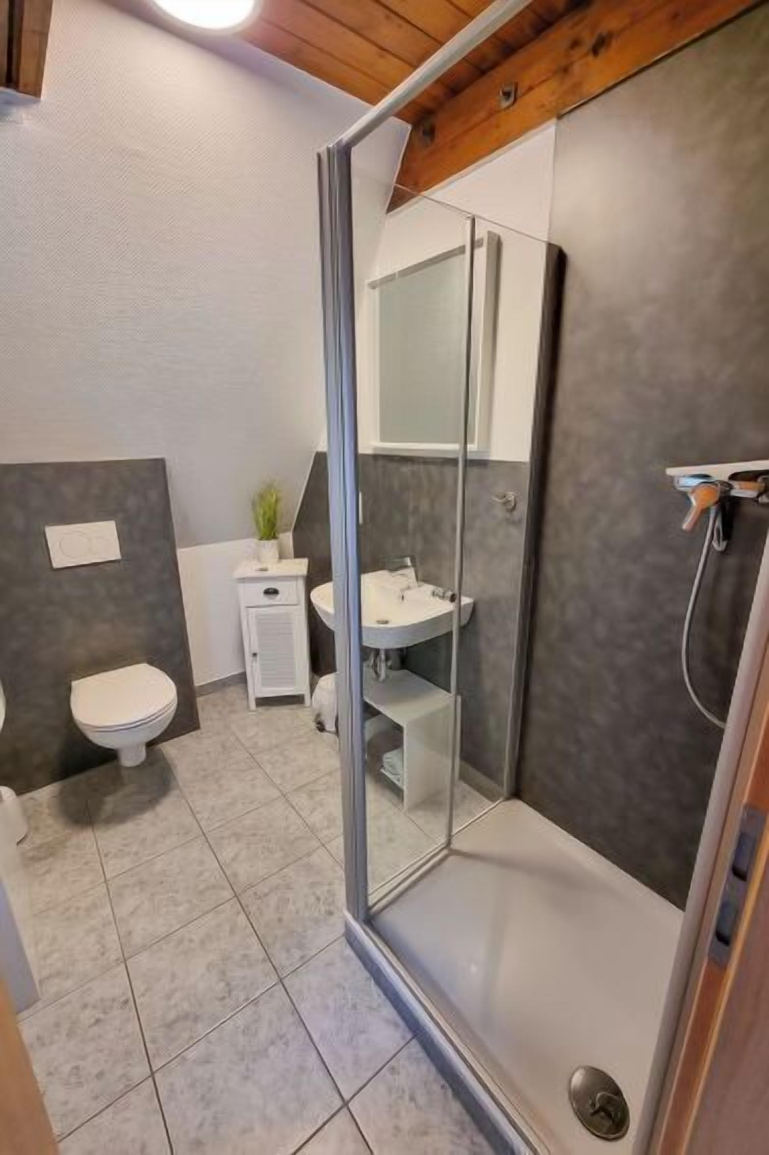 Moderni kylpyhuone, jossa on lasiseinällä varustettu suihku, valkoinen wc-istuin ja pieni pesualue.