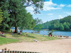 Un parc au bord du lac, doté d’aires de pique-nique, d’une plage de sable et d’un grand arbre qui offre de l’ombre.