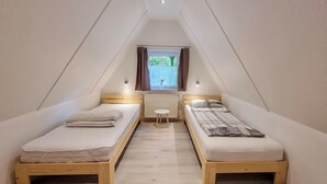 Un dormitorio ático pequeño y triangular con dos camas individuales, una mesita y una ventana con cortinas.