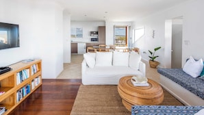A modern living room with a white sofa, a wooden bookshelf, a round coffee table, and a patterned sofa. - Little Beachies - Oceanstays (Angourie)