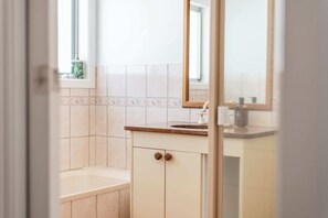 A bathroom with a bathtub, a sink with a mirror, and a window. - Little Beachies - Oceanstays (Angourie)