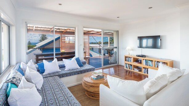A spacious living room with a large window, a sofa set, a coffee table, a bookshelf, and a flat-screen TV. - Beachies - Oceanstays (Angourie)