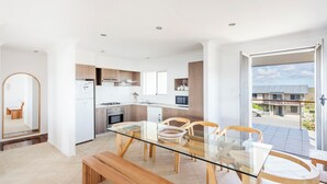 A modern kitchen with white cabinets, a glass dining table, and wooden chairs. - Beachies - Oceanstays (Angourie)
