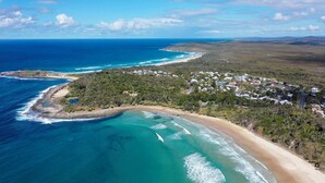 An aerial view of a coastal area with a beach, a small town, and a clear blue ocean. - Beachies - Oceanstays (Angourie)