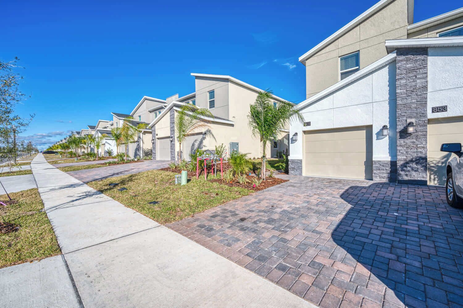 A row of modern townhouses with a paved driveway and a clear blue sky.