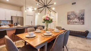 A modern kitchen with white cabinets, a stainless steel refrigerator, and a dining area with a wooden table set for four.