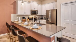 A modern kitchen with white cabinets, stainless steel appliances, a central island with bar stools, and pendant lighting.