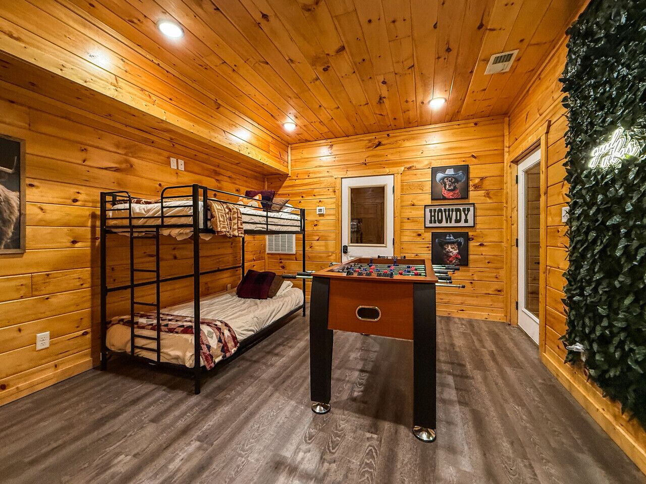 Ein Holzhütten-Zimmer mit Stockbetten, einem Kicker und einer Tür mit einem Neonzeichen.