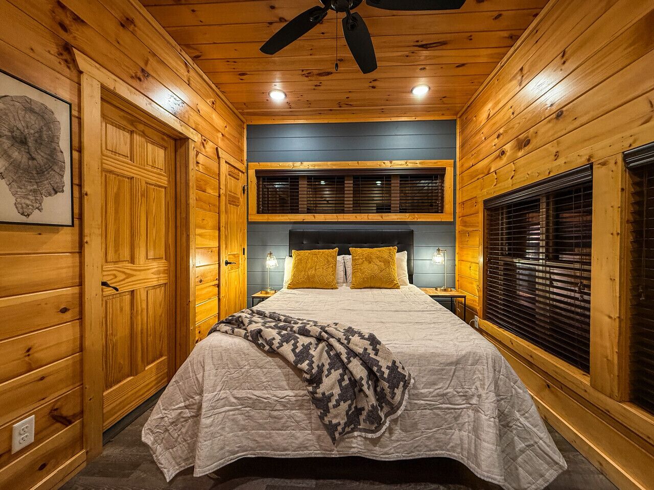 Une chambre confortable dans un chalet en rondins, avec un lit, des murs en bois, un ventilateur de plafond et une fenêtre avec des stores.