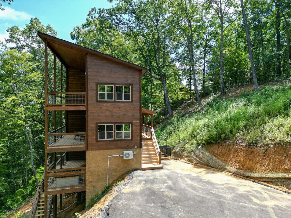 A two-story wooden cabin with a balcony, a staircase, and a concrete driveway.