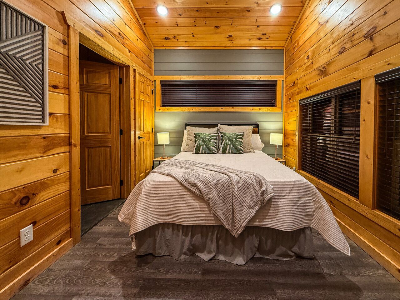 Quarto de cabana de madeira com cama, janela com persianas e porta.