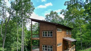 A multi-level wooden cabin with a balcony, surrounded by forest.