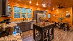 A wooden cabin interior with a kitchen featuring granite countertops, a central island, and a dining area with benches.