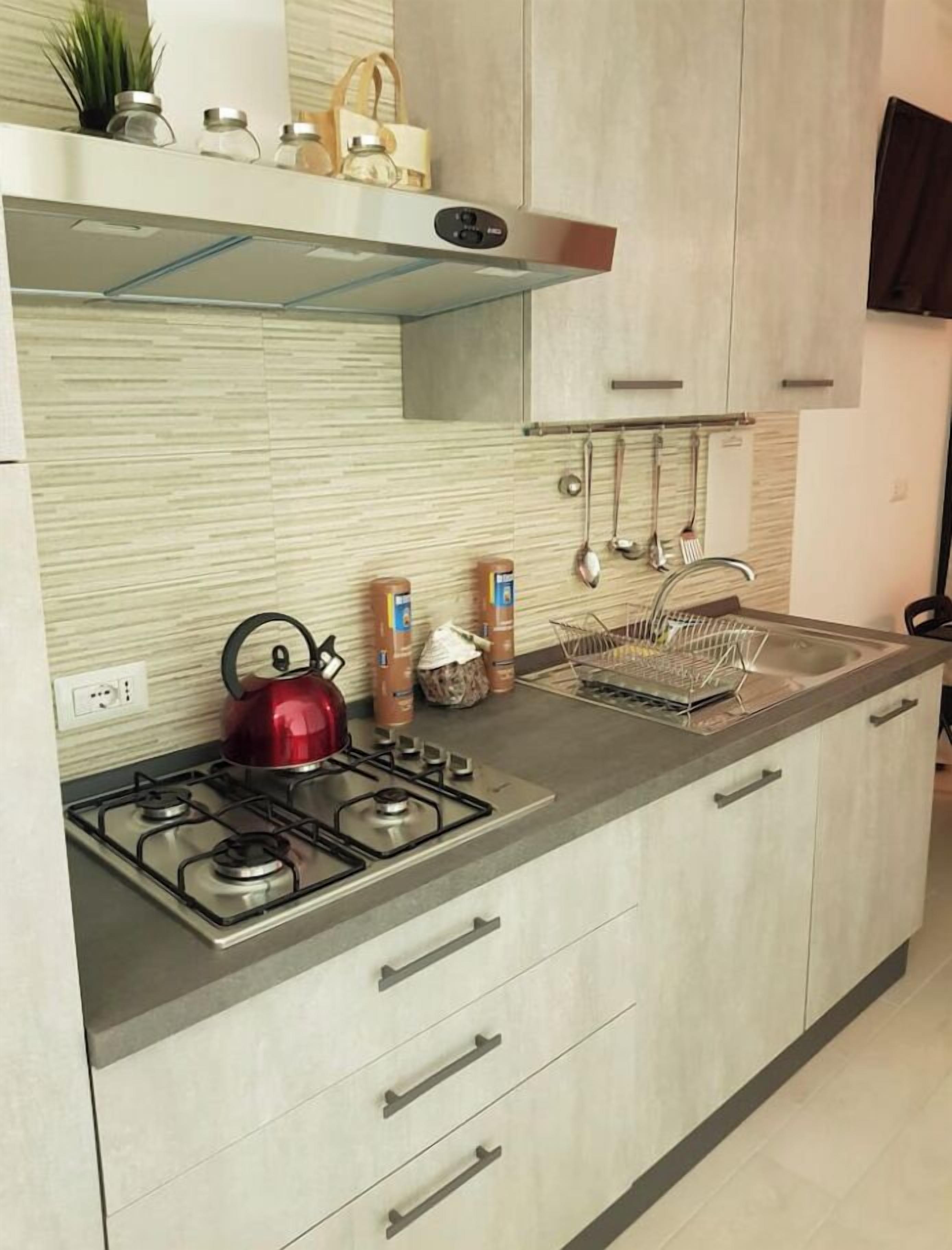A modern kitchen with a gas stove, kettle, and a stainless steel sink.
