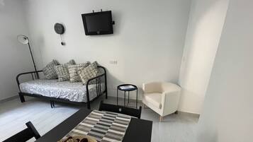 Una stanza moderna e accogliente con un letto, una televisione a parete, un piccolo tavolo con una ciotola di frutta, una sedia e una lampada.