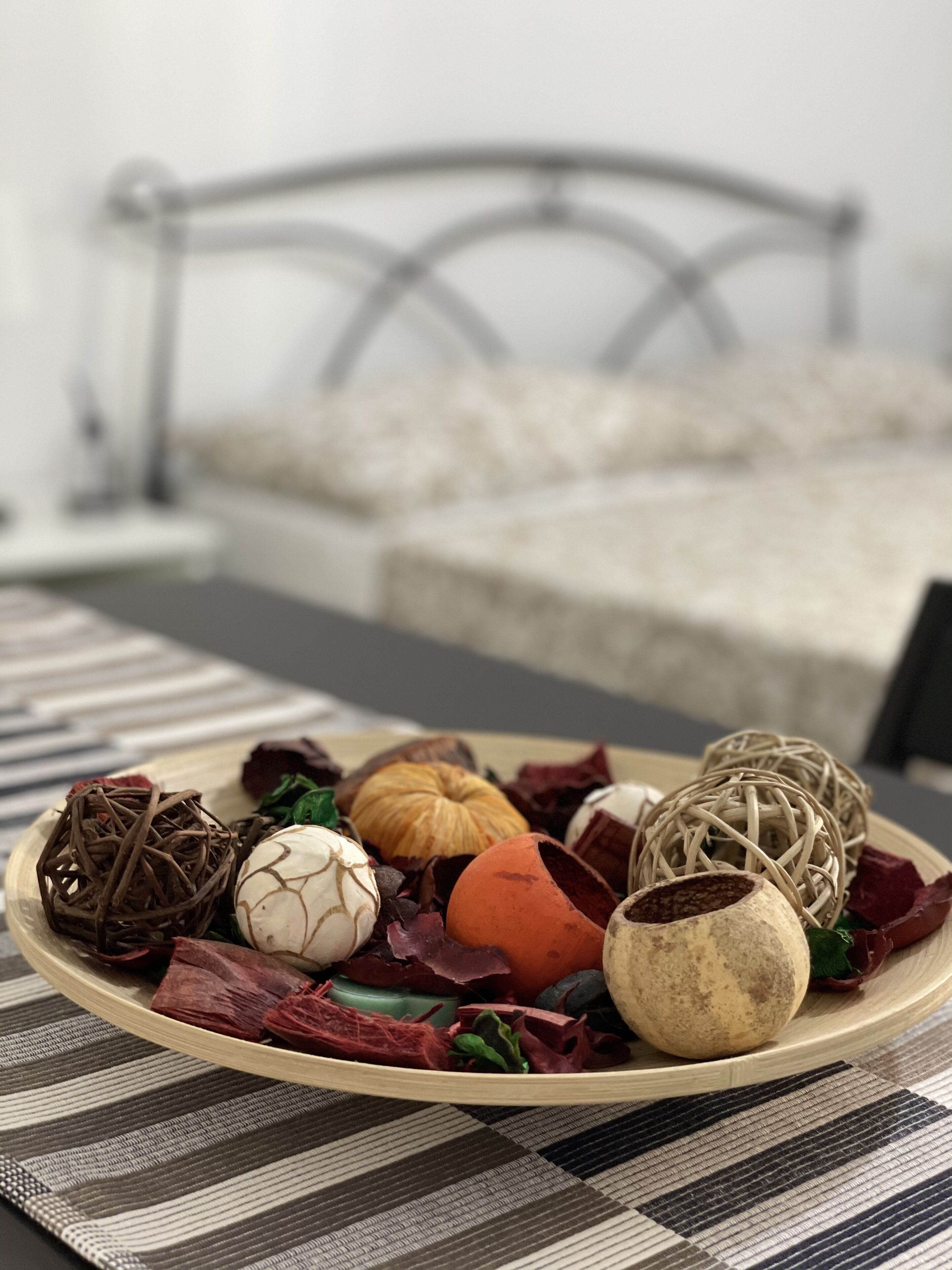 A bed with a metal frame and a wooden headboard, a wooden tray with decorative items, and a striped tablecloth.