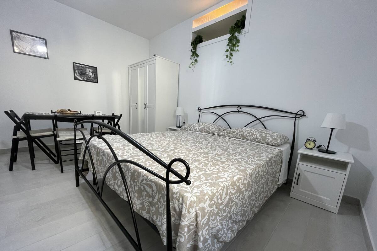 A bedroom with a bed, bedside table, lamp, and a desk with chairs.
