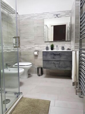 Ein modernes Badezimmer mit Duschkabine aus Glas, einem Bidet, einer Toilette, einem Waschtisch mit Spiegel und einem Handtuchhalter.