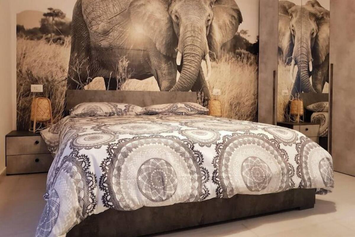 A bedroom with a large bed, patterned bedding, and two elephant-themed wall art pieces.