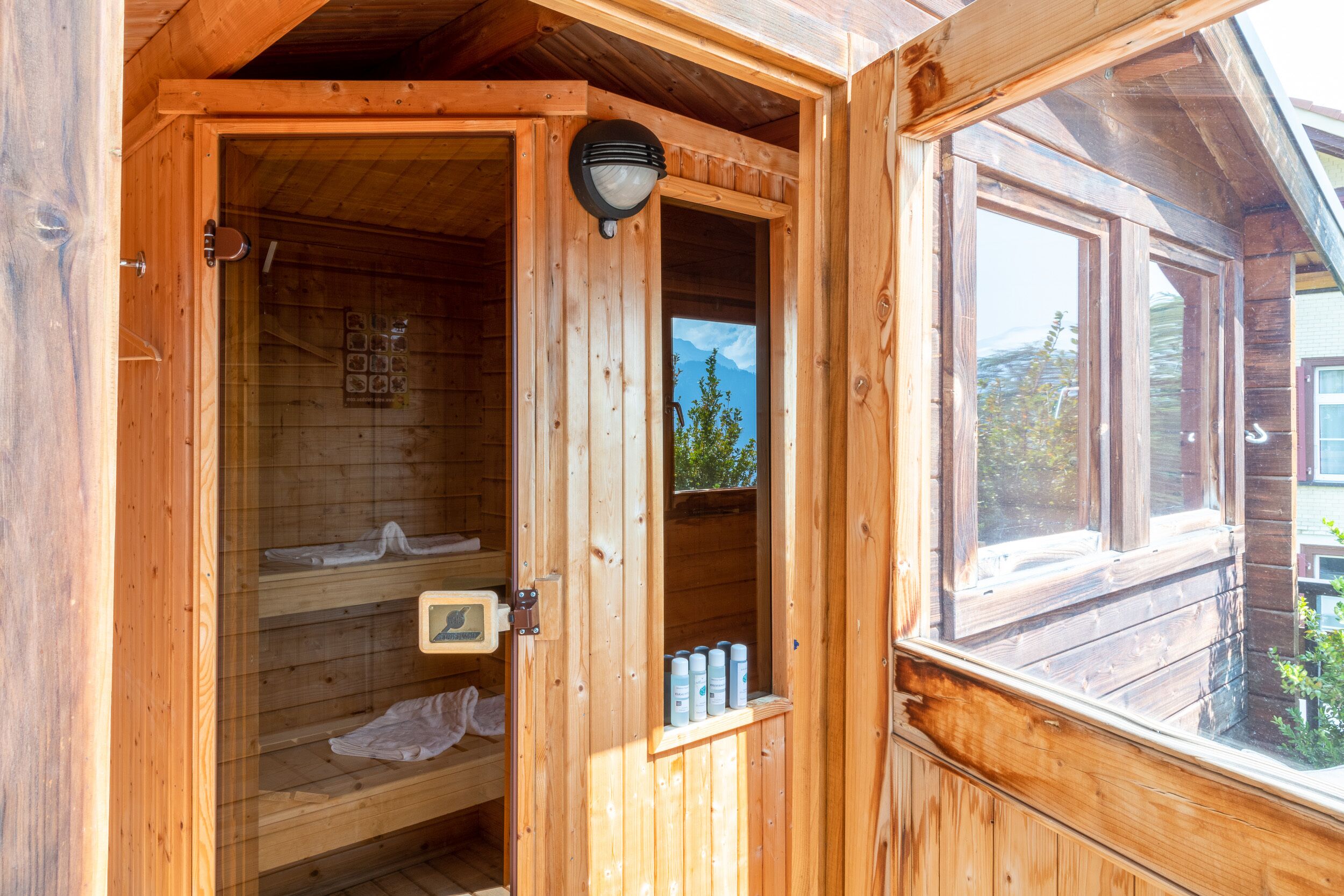 Eine Holzsauna mit Glastür, Handtuchhalter und Ablage mit Flaschen.