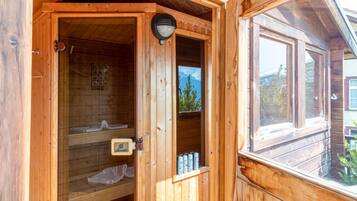 Eine Holzsauna mit Glastür, Handtuchhalter und Ablage mit Flaschen.