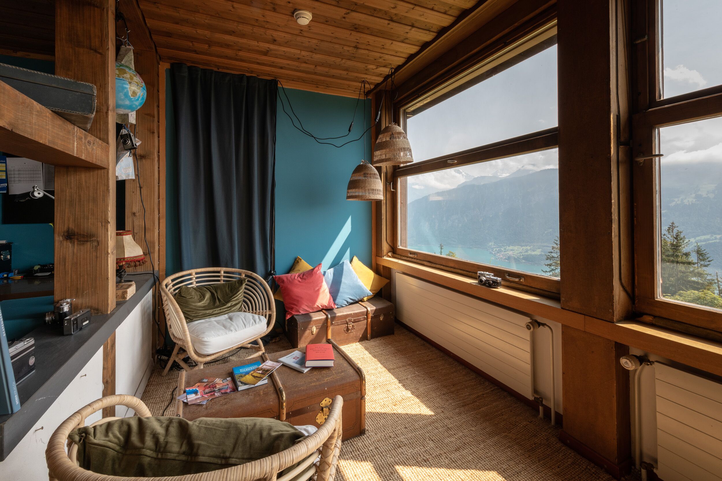 Una habitación acogedora con un amplio ventanal, mobiliario de mimbre y vistas a montañas.