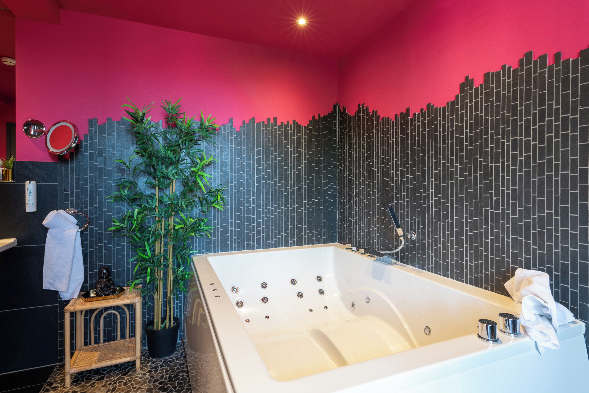 Een moderne badkamer met een groot bad, een potplant en een opvallend wandontwerp.